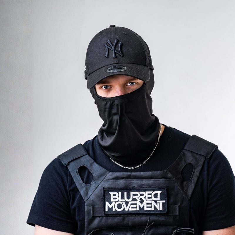 Blurred Movement, niederländischer Hard-Techno-DJ, mit schwarzer Sturmhaube, Cap und Weste mit Aufnäher